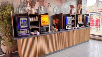 Un espace d’accueil avec un comptoir en bois, des machines à café et une fresque représentant des vases.