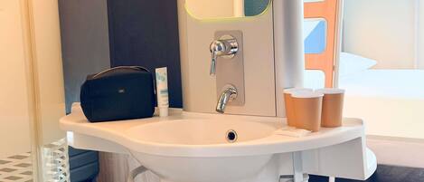 Un baño con un lavabo blanco, un espejo, una bolsa negra y una botella de loción.