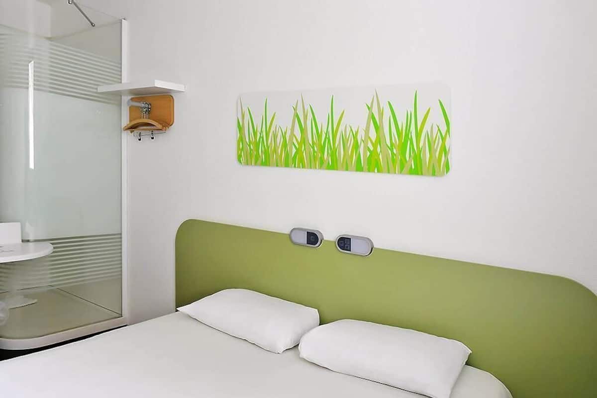 Ein modernes Hotelzimmer mit einem Bett, einer wandmontierten Digitaluhr und einer Duschkabine aus Glas.