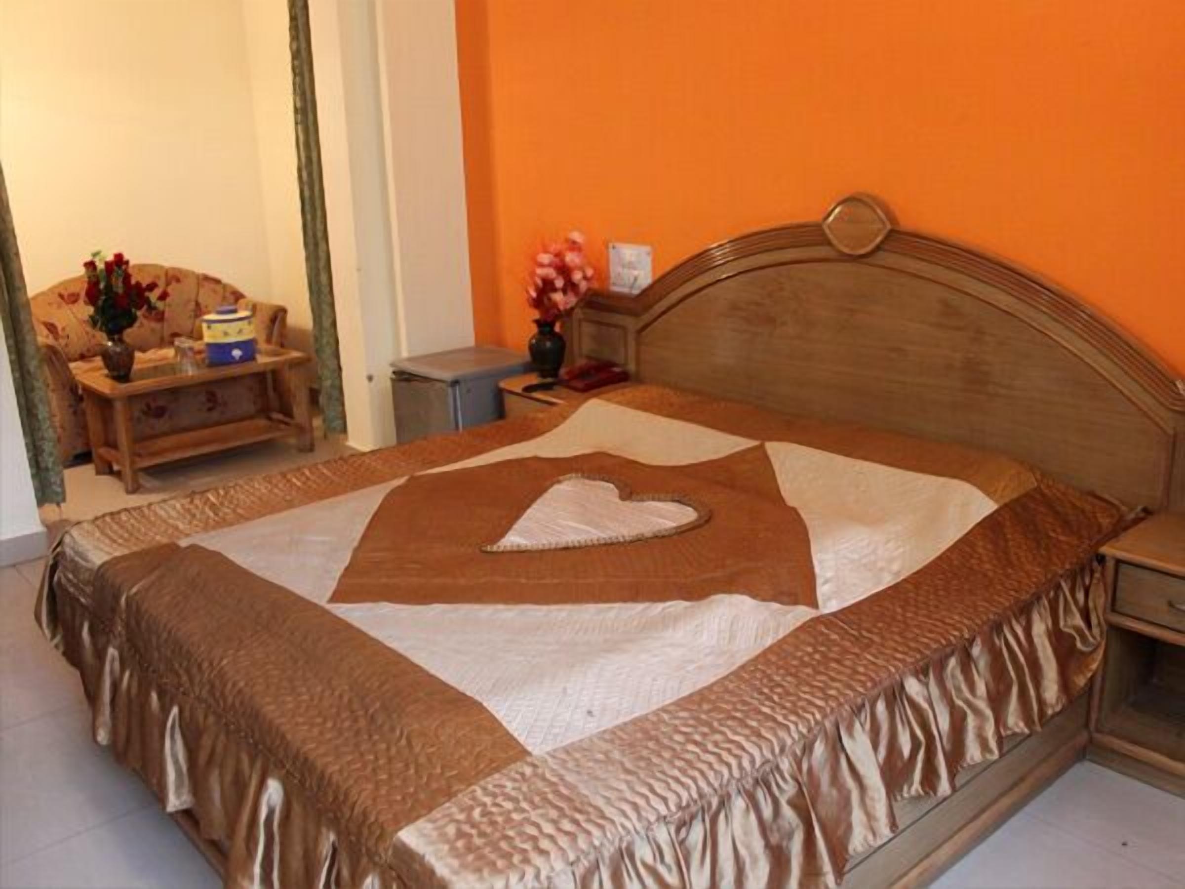 A neatly made bed with a heart-shaped pillow, a wooden headboard, and a bedside table with a vase of flowers.
