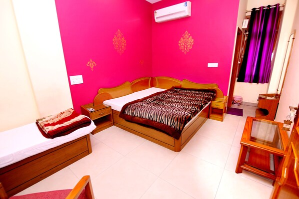 A bedroom with a bed, a bedside table, a chair, and a small wooden table. - Hotel Sunshine (Haridwar)