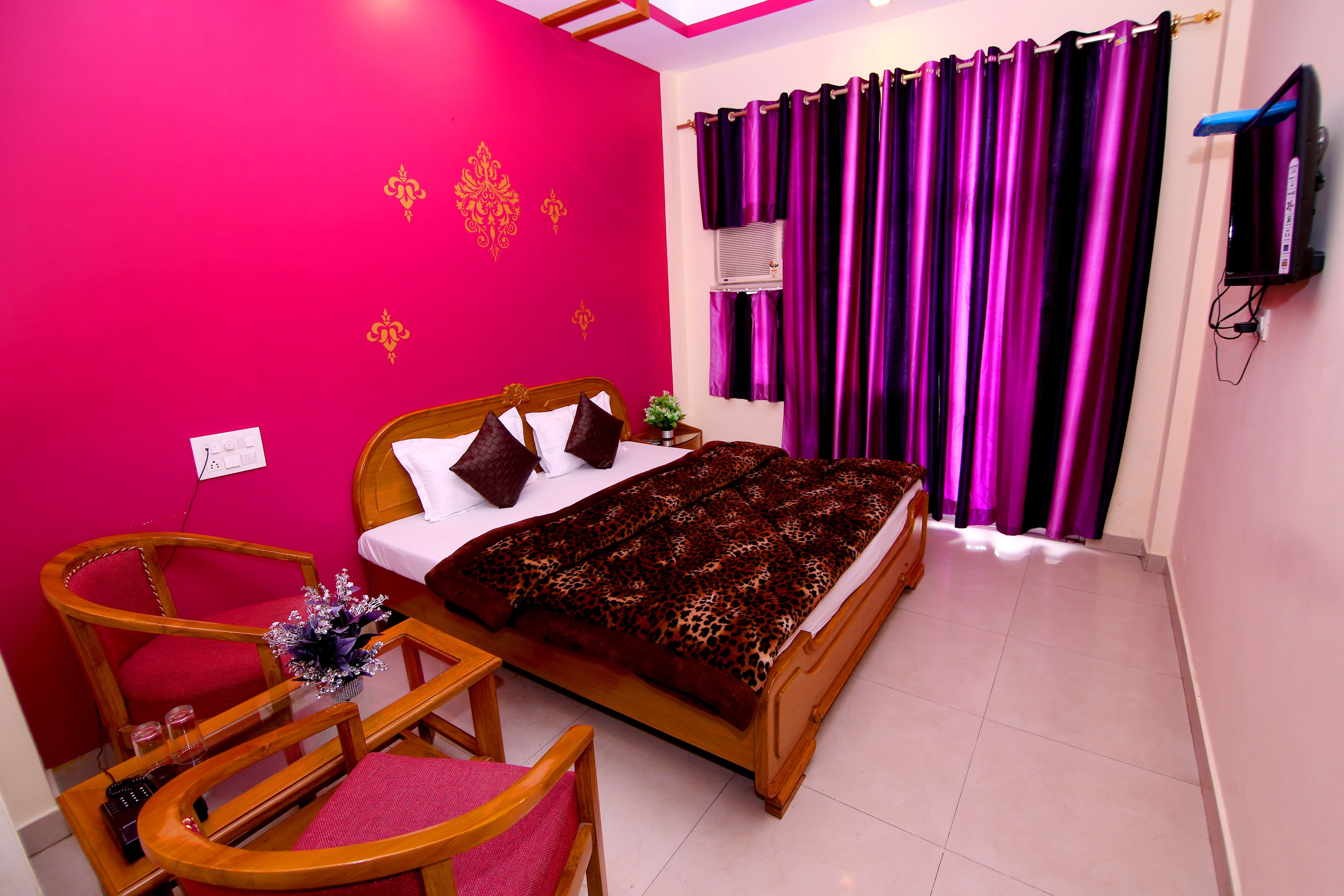 A bedroom with a bed, a wooden chair, a small table, and a TV on the wall.