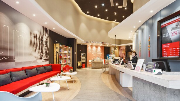 Un moderno vestíbulo de hotel con un mostrador de recepción, un sofá rojo, una estantería y una mesa de centro.