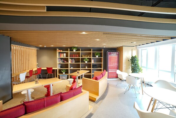 A modern hotel lobby with wooden paneling, a bookshelf, seating areas, and a reception desk. - ibis Chengdu West Jingcui Road (Chengdu)