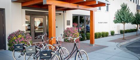 Een hotelingang met een overdekt terras, fietsen die buiten geparkeerd staan, en een goed onderhouden bloembed.