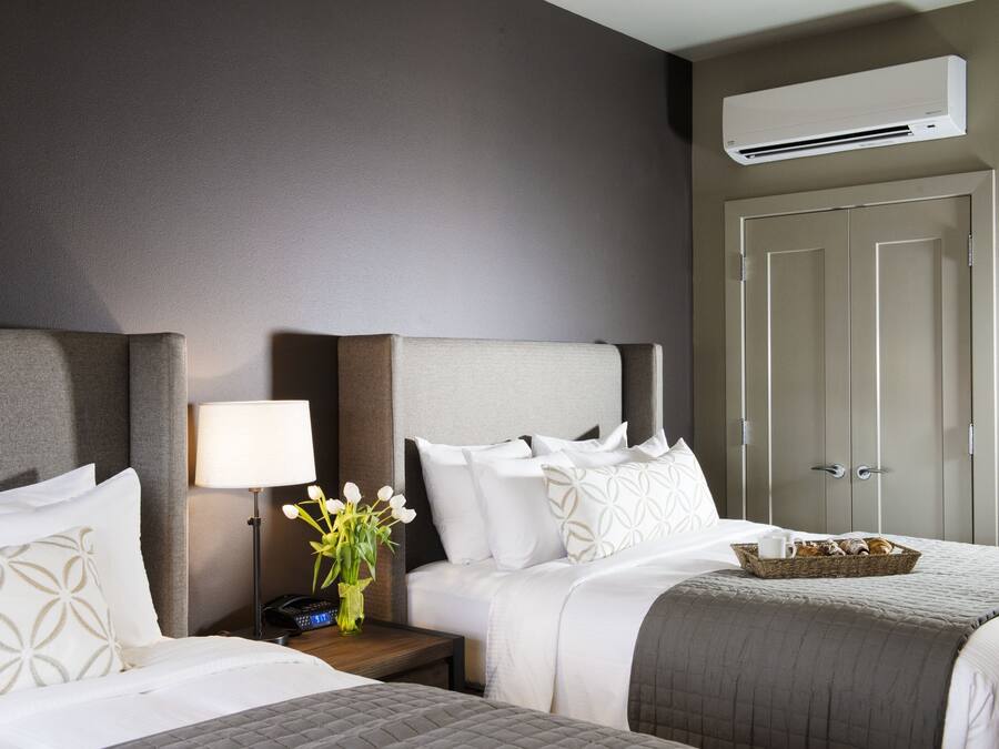 A hotel room with two beds, a nightstand with a lamp, a vase of flowers, and a basket of pastries.