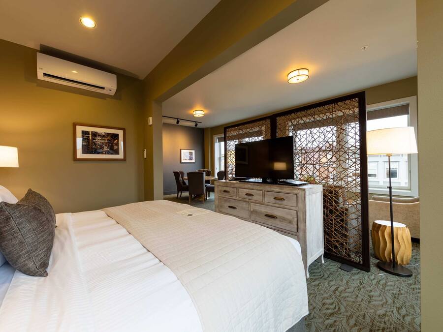 A hotel room with a large bed, a desk with a television, an air conditioning unit, and a decorative partition.