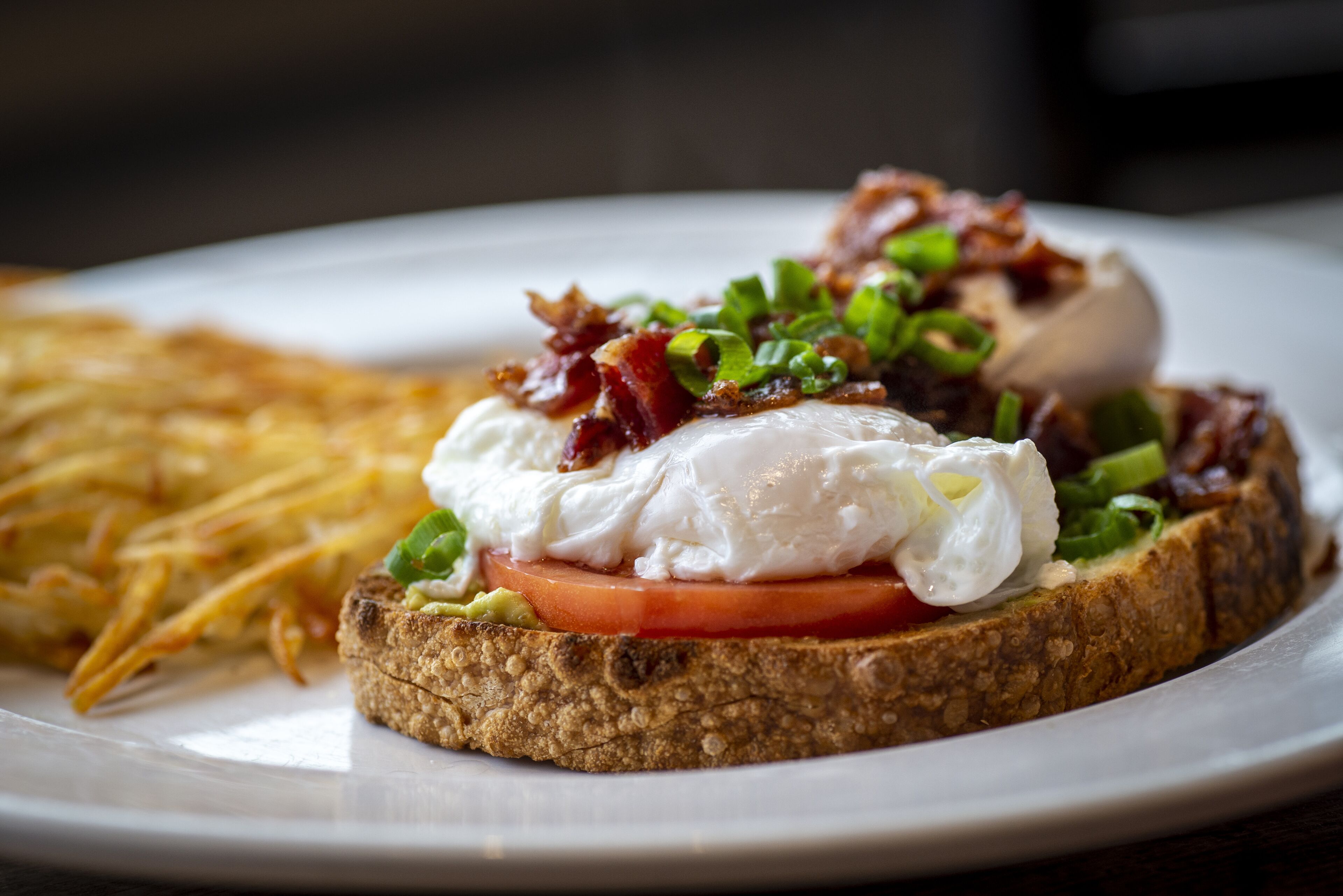 A plate with a sandwich topped with bacon, a poached egg, and green onions, alongside a side of fries.