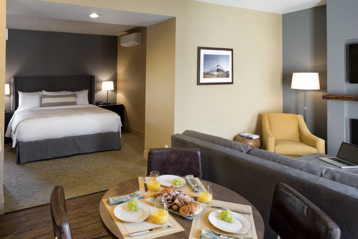 A hotel room with a bed, a sofa, a dining table with breakfast, and a TV.