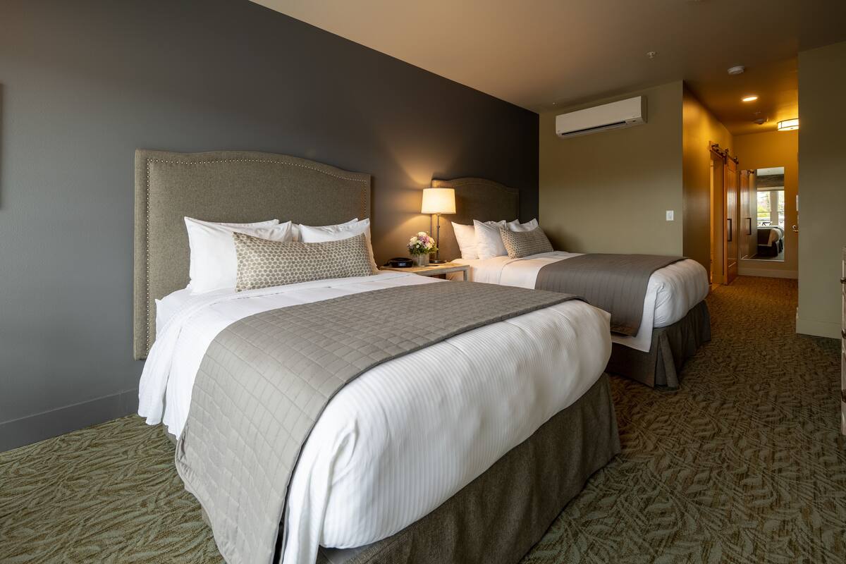 A hotel room with two beds, a nightstand with a lamp, and a carpeted floor.