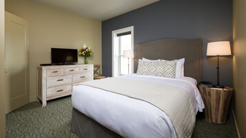 Una habitación de hotel con cama, cómoda, televisor, lámpara y un florero con flores.