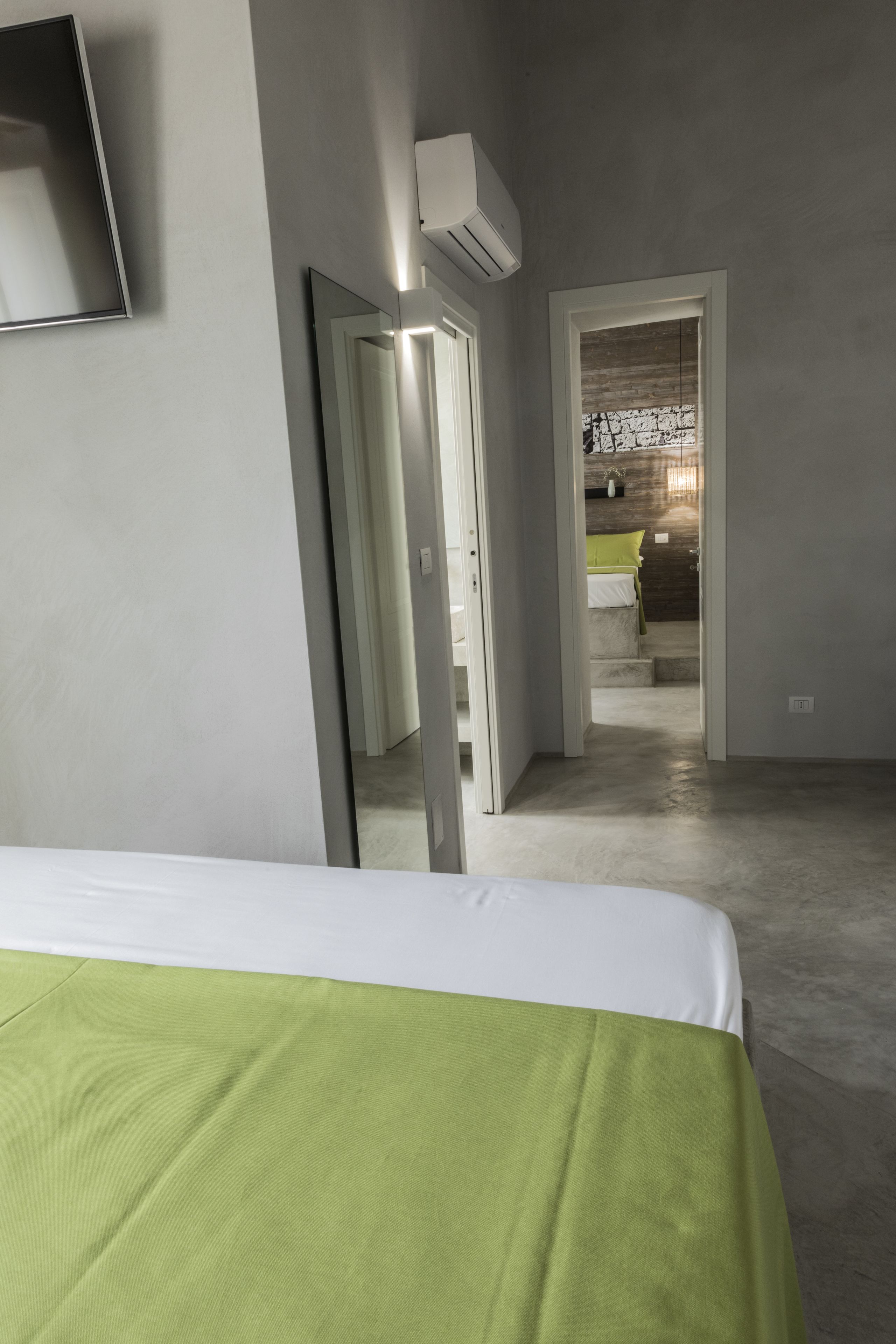 A bedroom with a bed, a mirror, and a hallway leading to a bathroom.