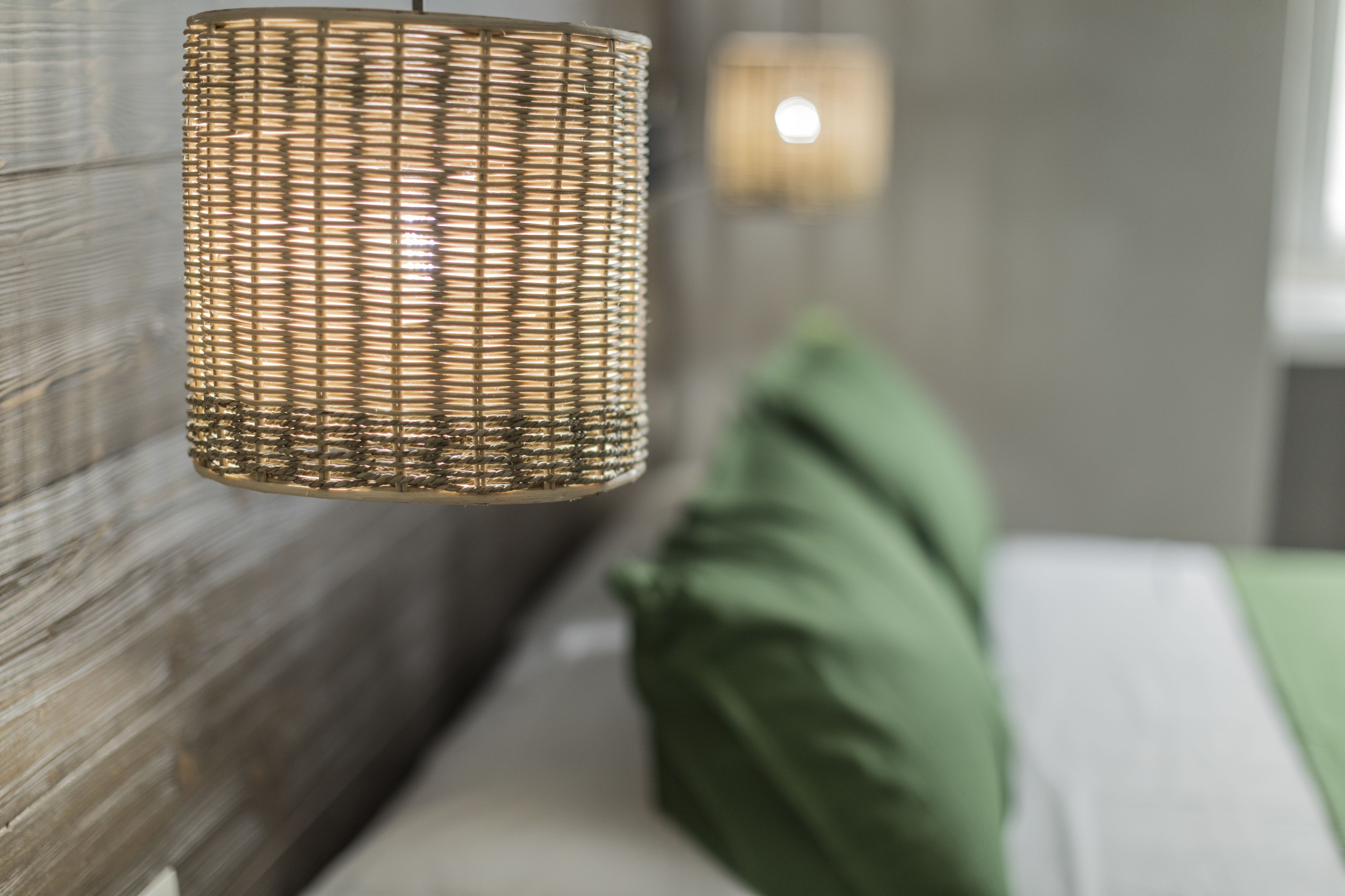 A wicker lamp hanging from a wall in a room with a green pillow on a bed.