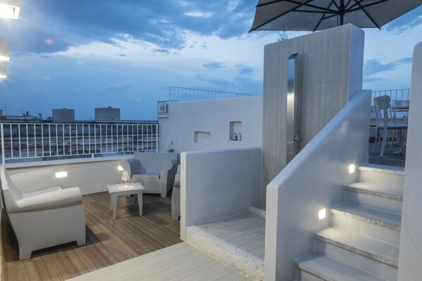 Una terrazza sul tetto con arredi bianchi, un piccolo tavolo con un bicchiere e una scala.