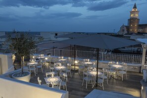 Una terrazza esterna con tavoli e sedie, una pianta in vaso e vista su una torre.