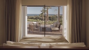 Camera da letto con un'ampia porta scorrevole in vetro che si apre su un patio esterno con vista sull'oceano e sulle palme.