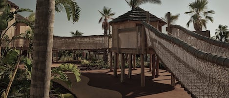 A wooden structure with a thatched roof, surrounded by a rope barrier and palm trees.