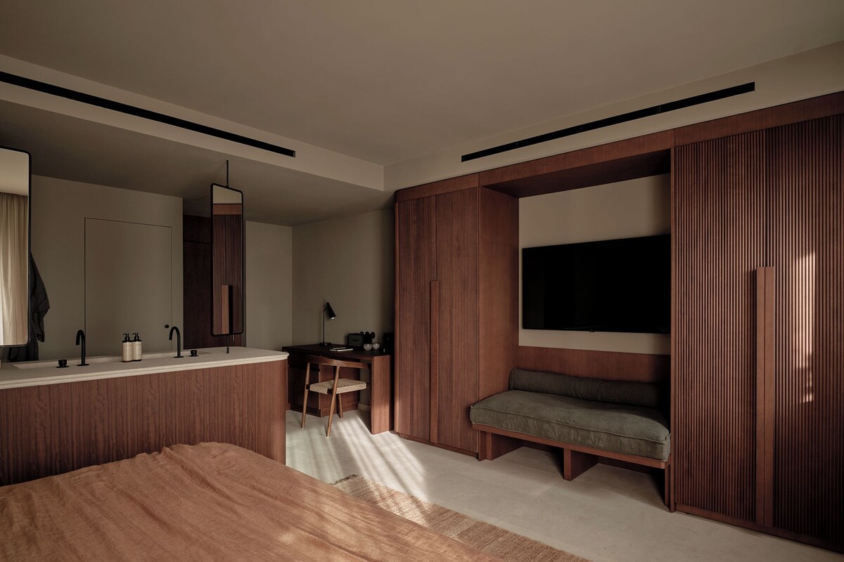 A modern bedroom with a large bed, a vanity with a mirror, a desk, and a television mounted on the wall.