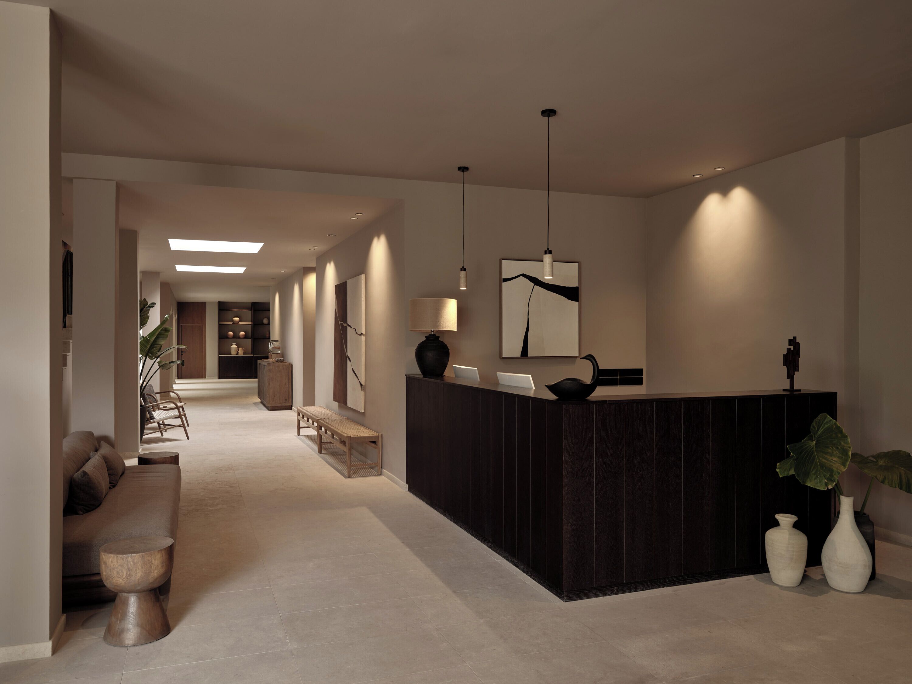 Un área de recepción moderna con un mostrador oscuro, iluminación colgante y una decoración minimalista.