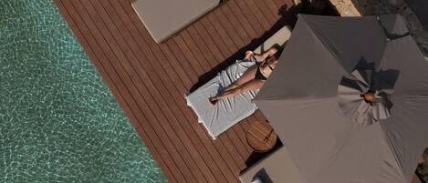 A wooden deck with lounge chairs and a large umbrella, overlooking a clear blue pool.