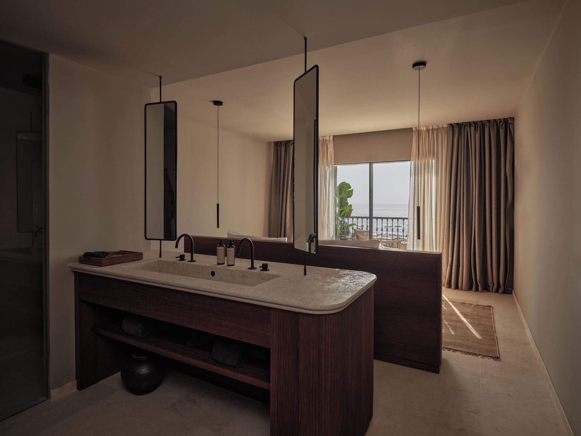 Une salle de bain moderne avec un grand lavabo, deux miroirs et une vue sur la mer par la fenêtre.