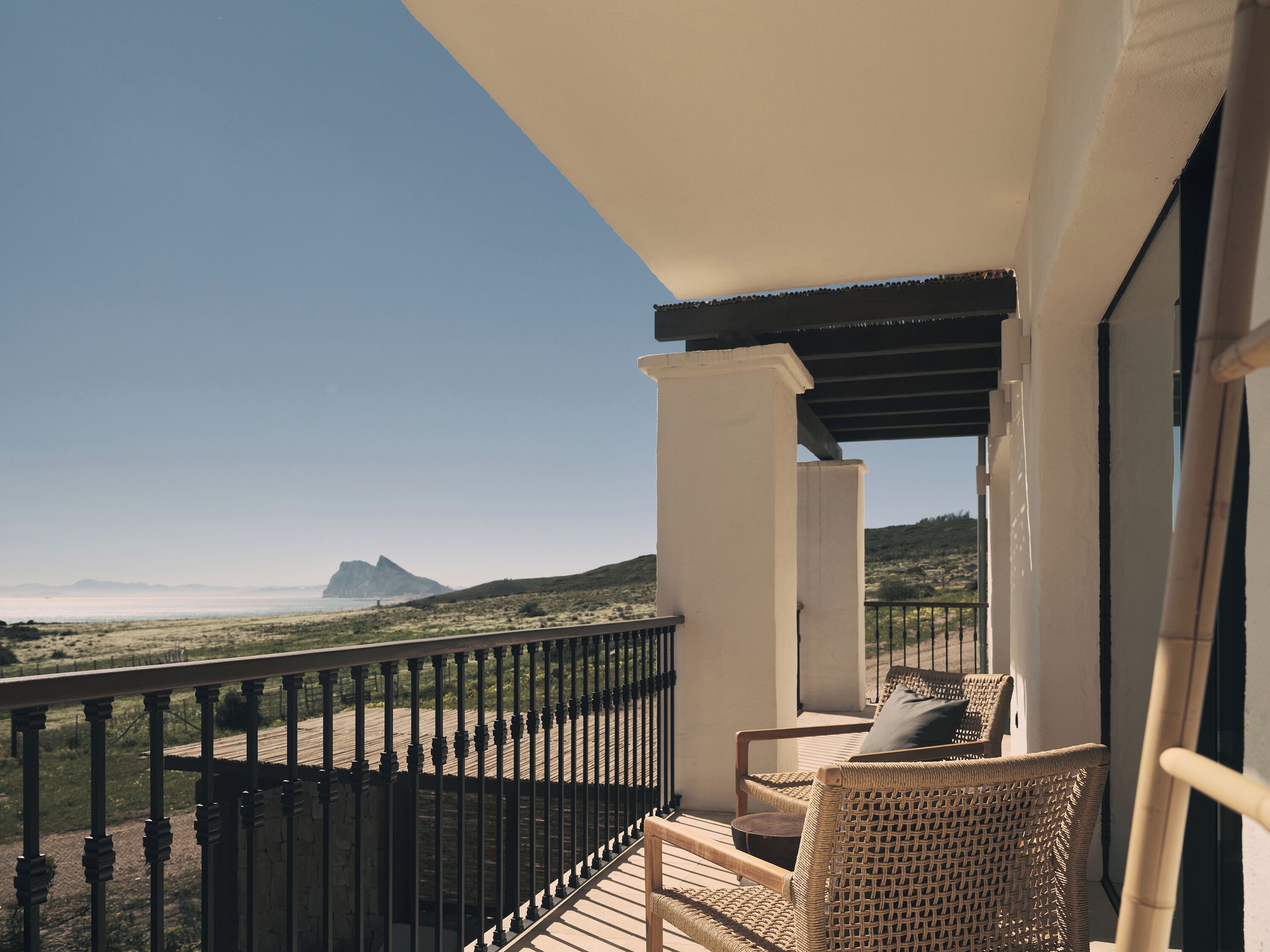 Un balcón con muebles de mimbre, vistas al paisaje y una montaña al fondo.