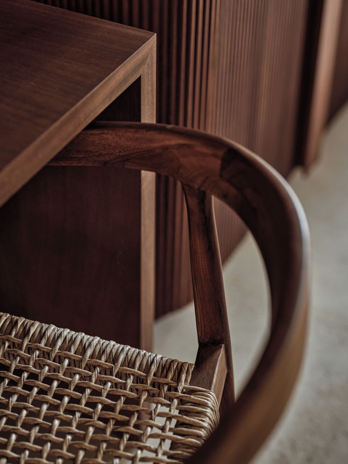 Primer plano de una silla de madera con asiento y respaldo trenzado, colocada junto a una mesa de madera.