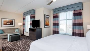 A hotel room with a bed, a TV, a sofa, a desk, and a window with curtains.