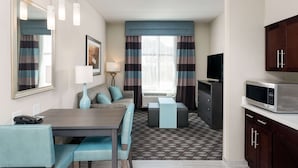 A compact hotel room with a dining area, kitchenette, and a large window with striped curtains.
