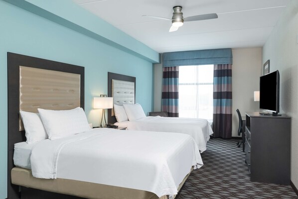 Ein Hotelzimmer mit zwei Betten, einem Schreibtisch, einem Fernseher und einem Deckenventilator.