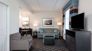 Une chambre d’hôtel avec un canapé, un fauteuil, une télévision et une moquette à motifs.