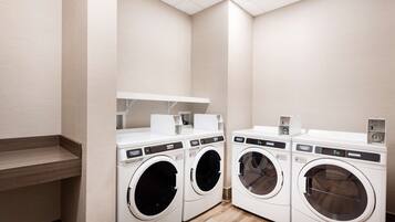 A laundry room with three front-loading washing machines and a shelf above them.