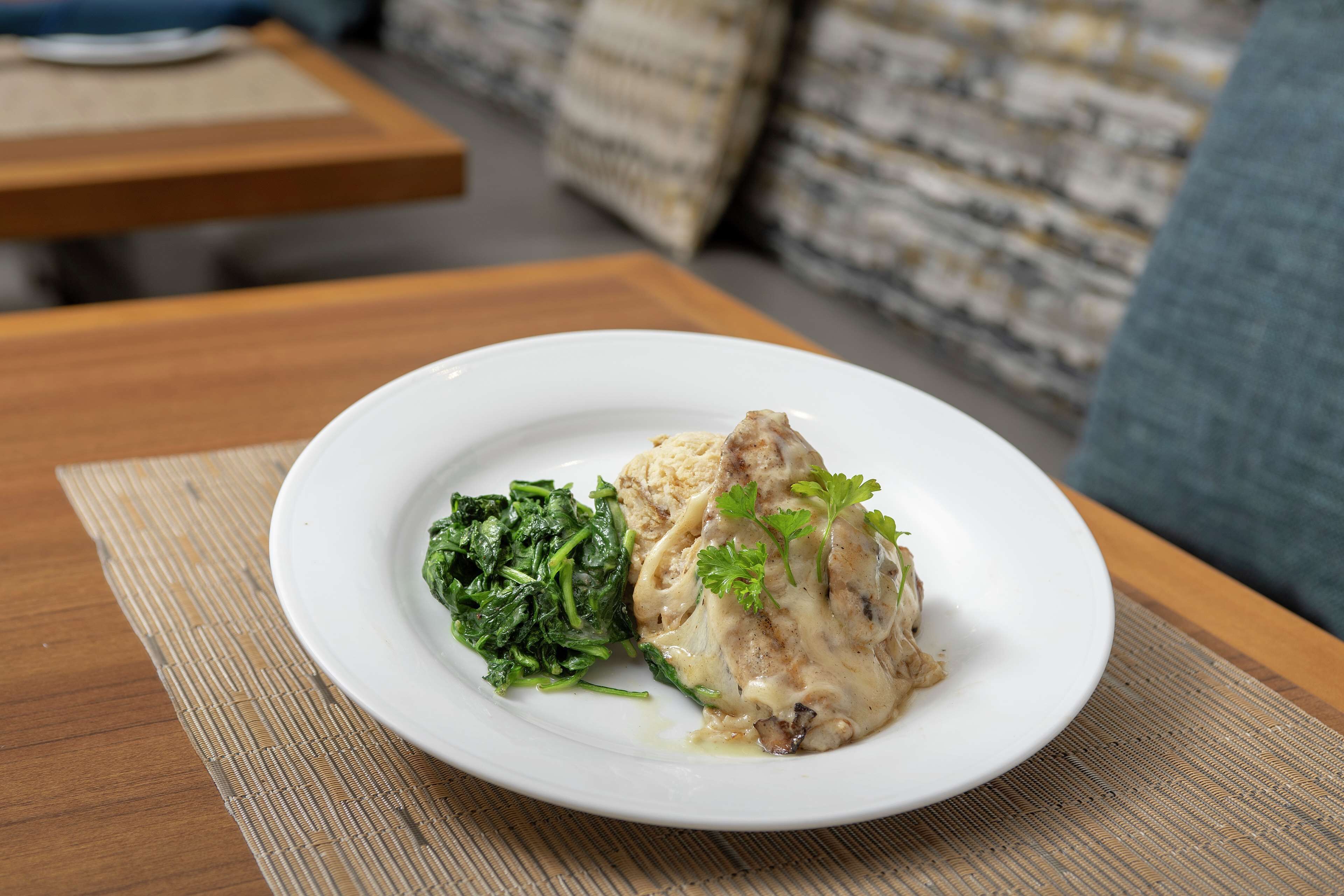 A plate with a white meat dish and greens on a wooden table.