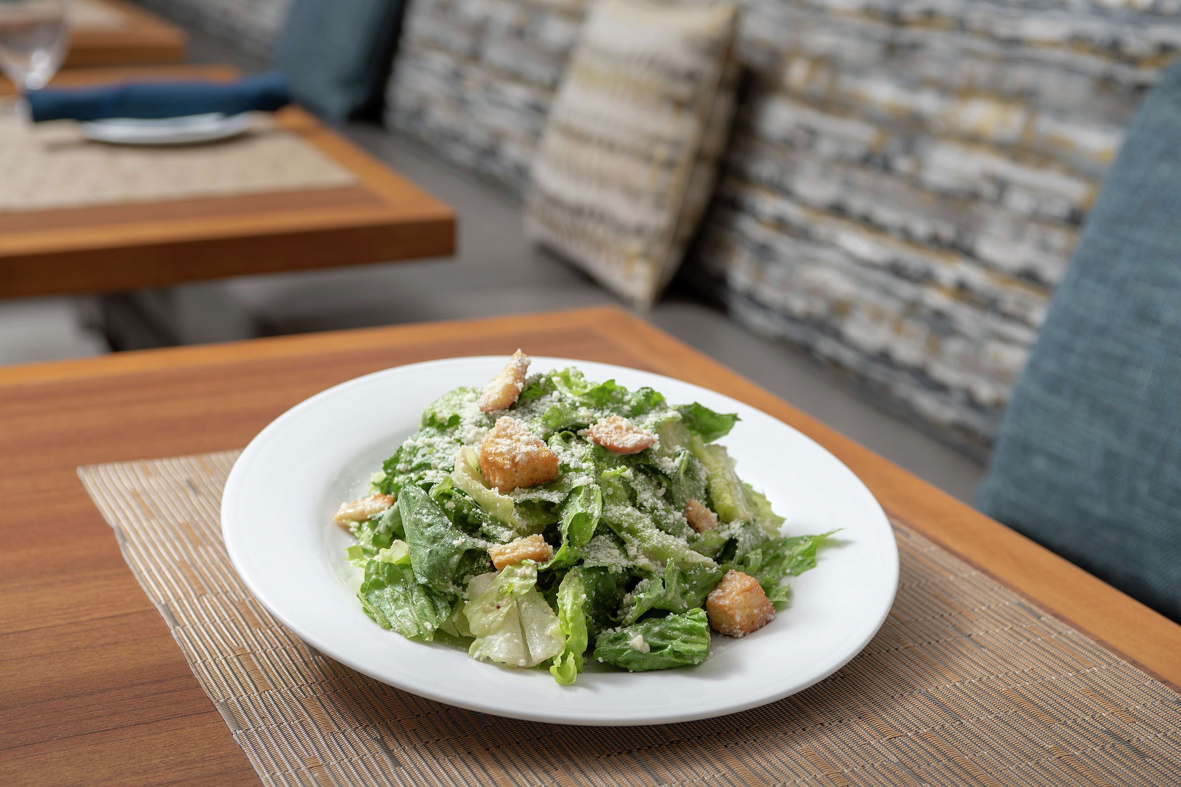 Een bord Ceasar salade op een houten tafel met een geweven tafelonderzetter.