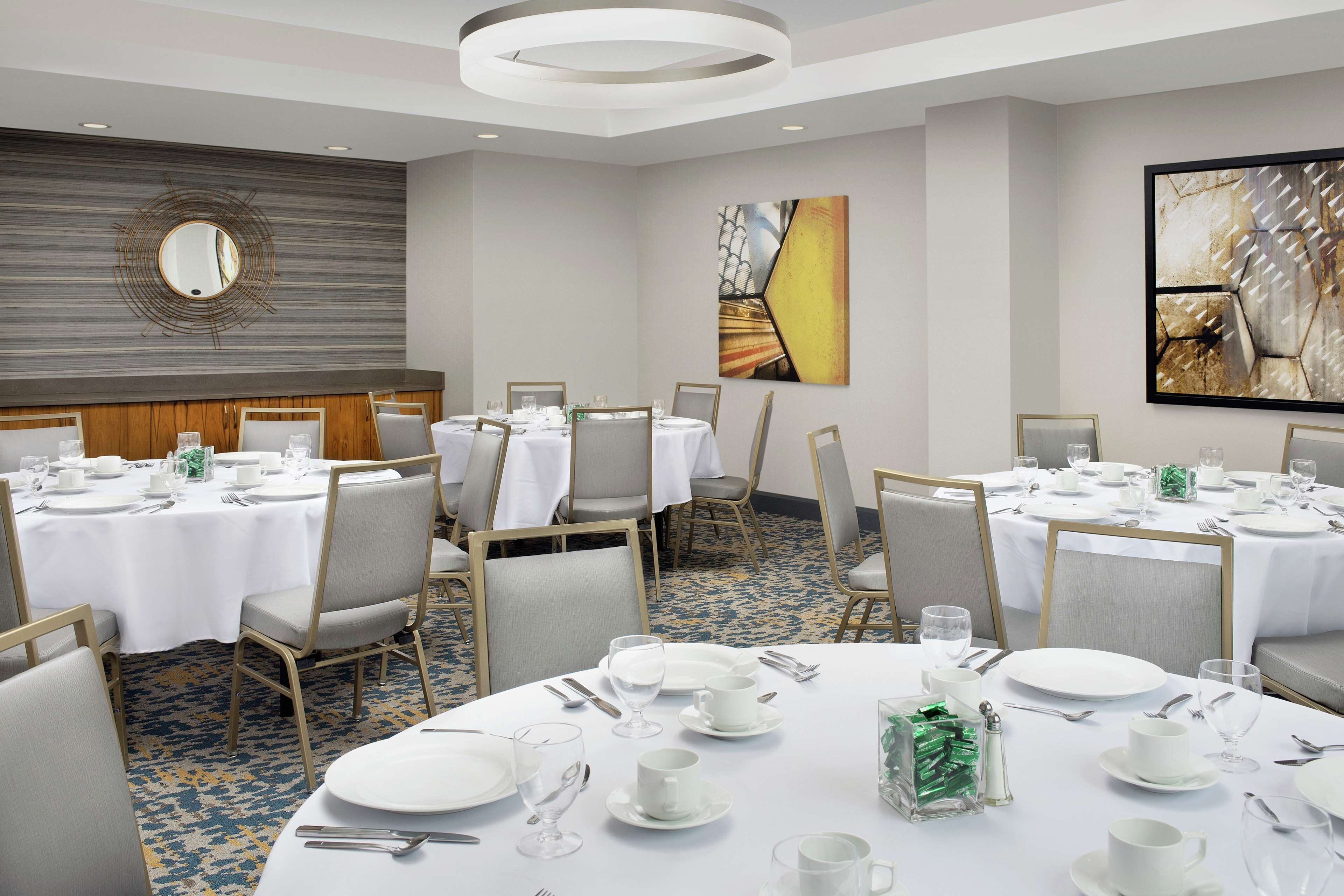 A conference room with multiple round tables set for dining, equipped with white tablecloths, chairs, and dining utensils.