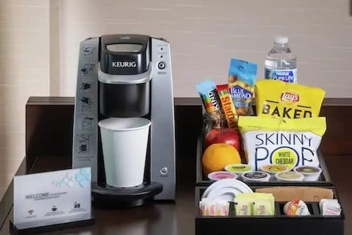 Una cafetera, un cartel de bienvenida y una bandeja con aperitivos y condimentos.
