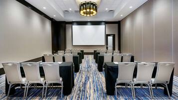 A conference room with rows of white chairs, a large screen, and a patterned carpet.