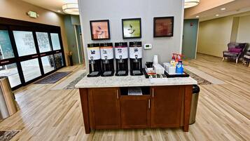A coffee station with multiple dispensers, a small refrigerator, and a tray with condiments and napkins.