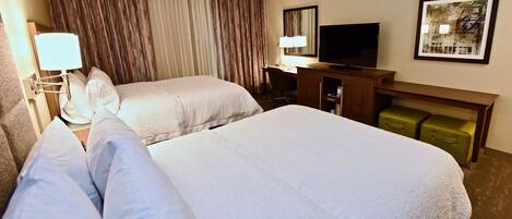 A hotel room with two beds, a desk with a chair, a television, and a framed picture on the wall.