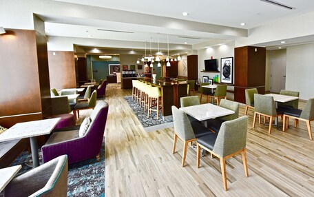 A modern hotel lobby with multiple seating areas, including a bar and dining tables.