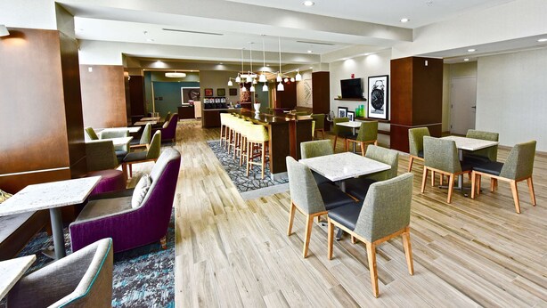 Un moderno vestíbulo de hotel con varias zonas de estar, incluyendo un bar y mesas de comedor.