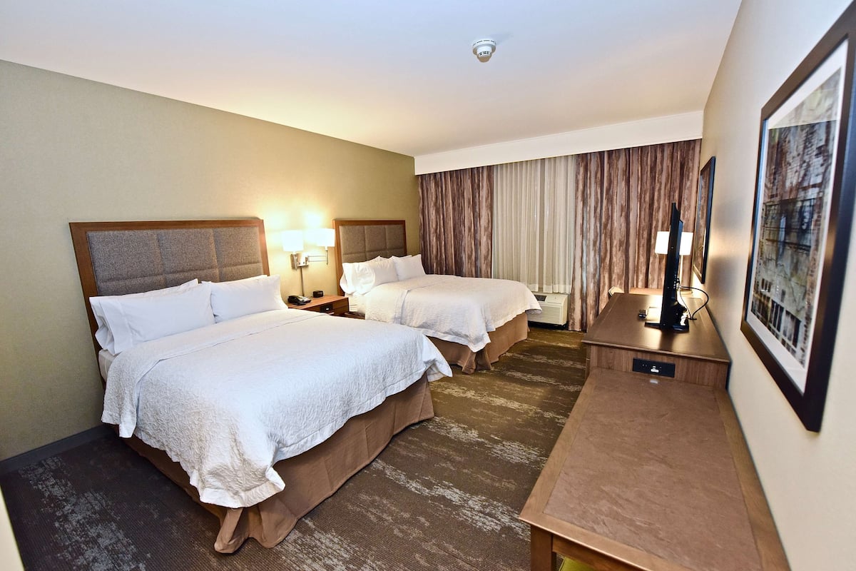 A hotel room with two beds, a desk, a lamp, and a painting on the wall.