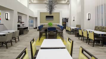 Un comedor amplio con varias mesas y sillas, una planta en el centro y una lámpara moderna.
