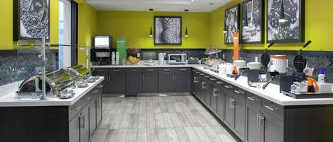 A modern kitchen with grey cabinets, a white countertop, and a microwave. There are framed pictures on the wall and a coffee machine on the counter.