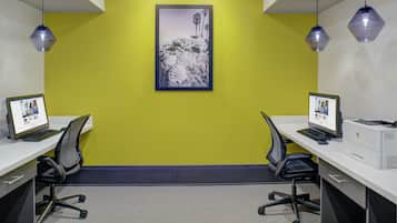 A workspace with two desks, each with a computer and chair, against a yellow wall with a framed picture.