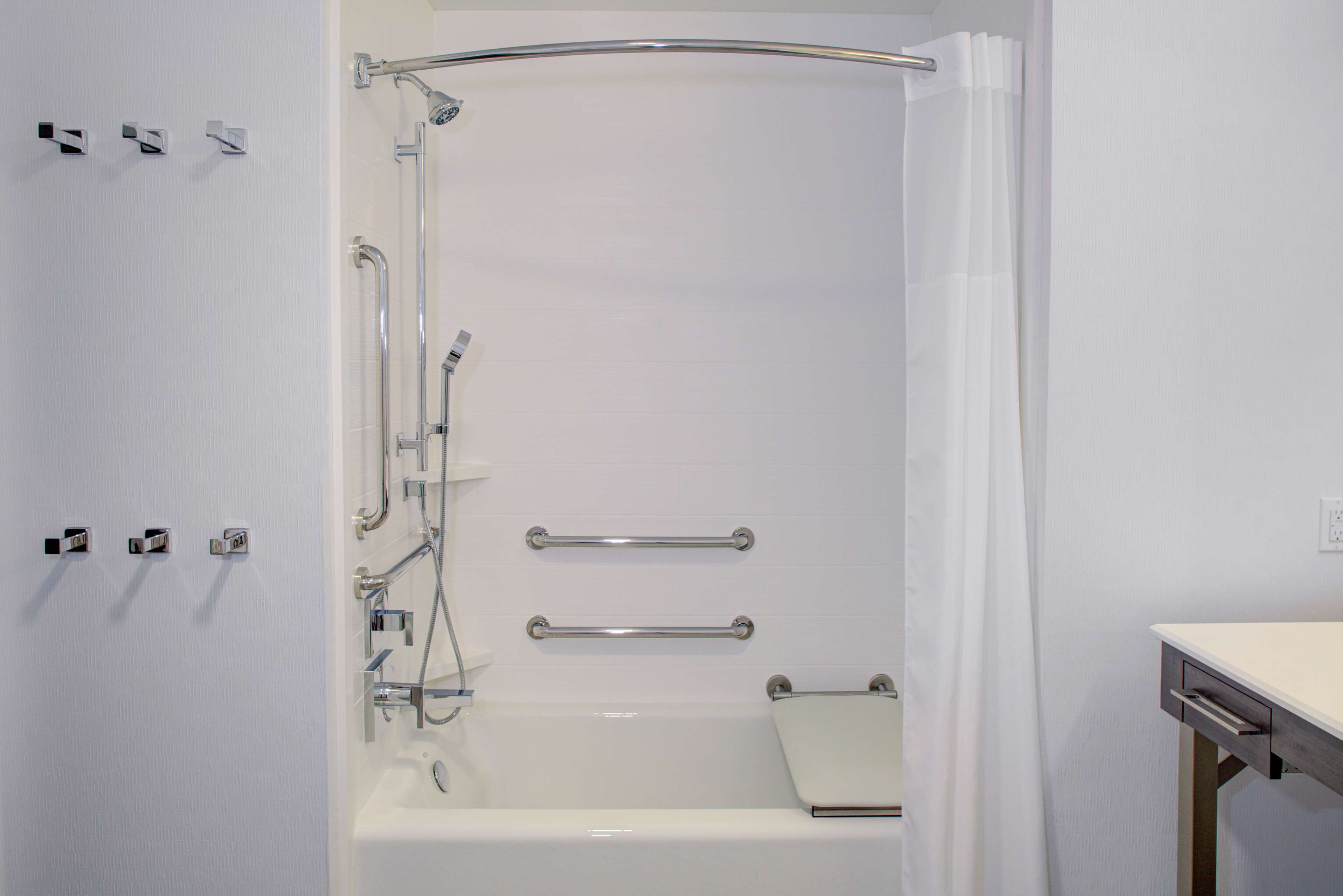 A modern bathroom with a walk-in shower, grab bars, and a white sink.