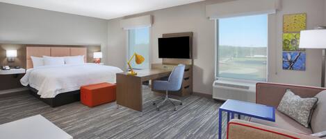 A hotel room with a bed, desk, chair, TV, and a couch.
