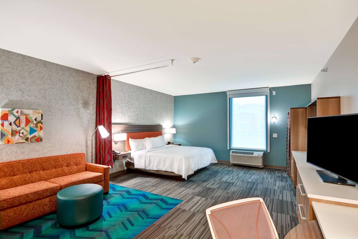 A hotel room with a bed, a sofa, a desk, a TV, and a window.