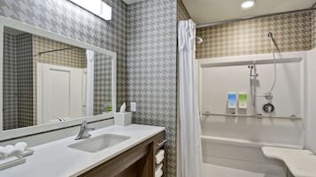 A modern bathroom with a large mirror, dual sinks, a shower with a handheld showerhead, and a towel rack.