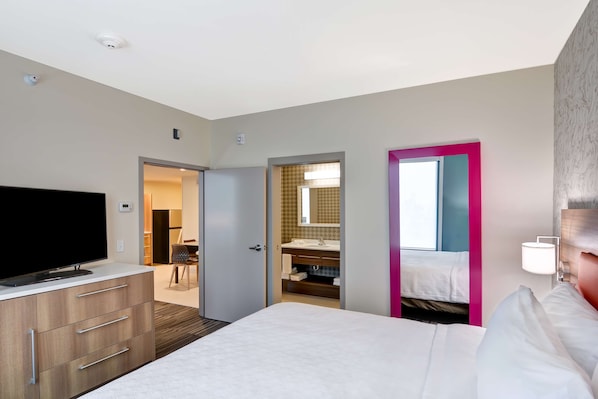 Habitación de hotel con cama, televisor en una cómoda, baño con espejo y puerta que da a otra habitación.